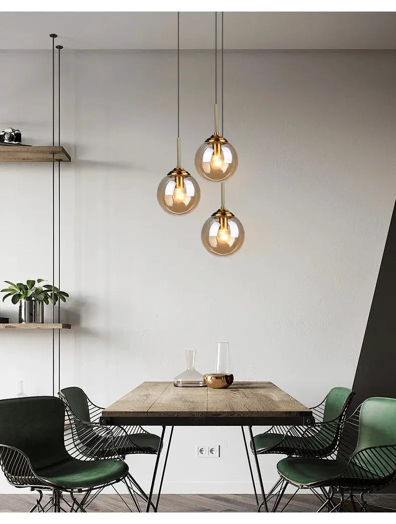 Nordic-inspired three glass globe pendant lights with brass hardware and LED bulbs over a wooden dining table