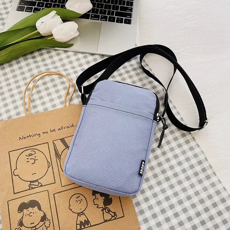 Light blue vertical crossbody messenger bag by Simples Market with black adjustable strap and zipper pocket