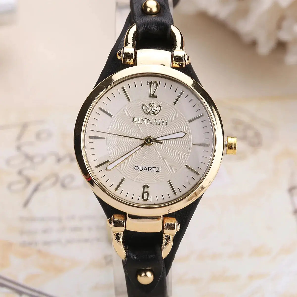 RINNADY quartz women's watch with gold-tone case, white dial, and black leather strap.