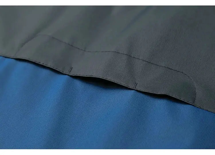 TRVLWEGO men's outdoor jacket color-block: black upper panel over blue body, close-up seam detail.