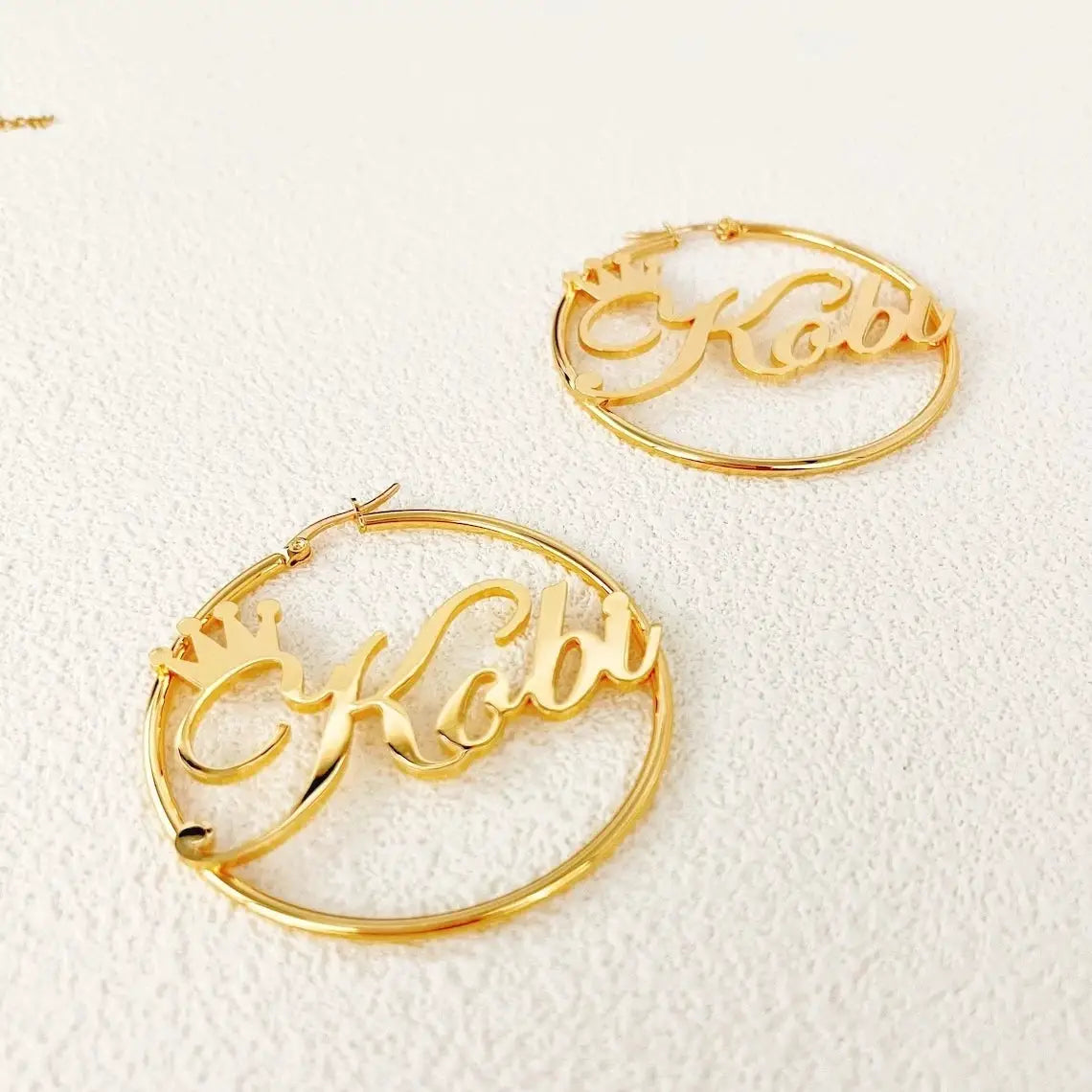Pair of gold-tone stainless steel crown-name hoop earrings with scripted name by Simples Market