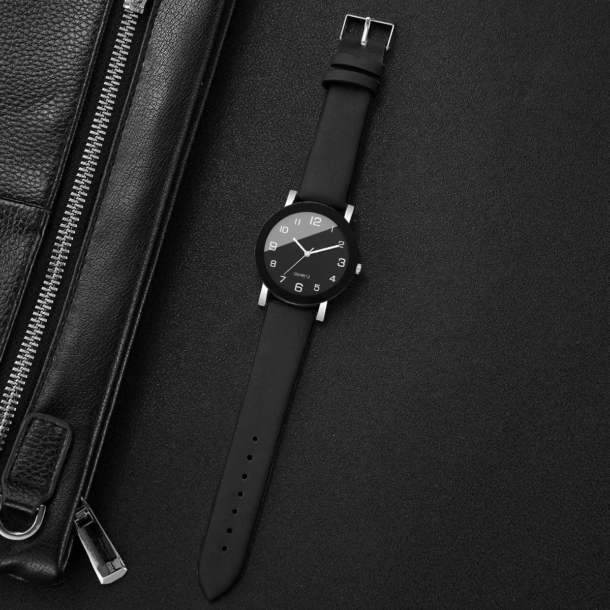 Wristwatch with black leather strap and black dial with white Arabic numerals.