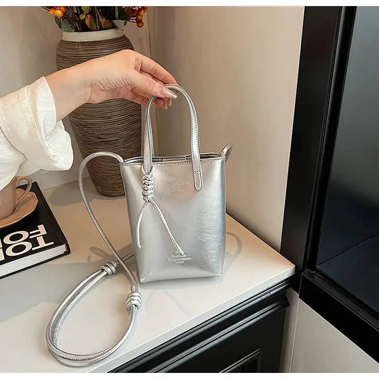 Silver mini PU leather crossbody bag with top handle, long adjustable strap, and knotted tassel accent.