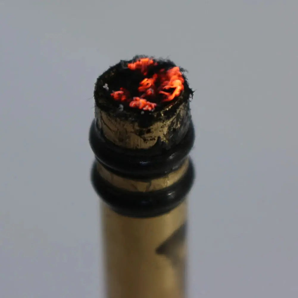 Brass emergency fire tube igniter with glowing red ember and charred top for camping.