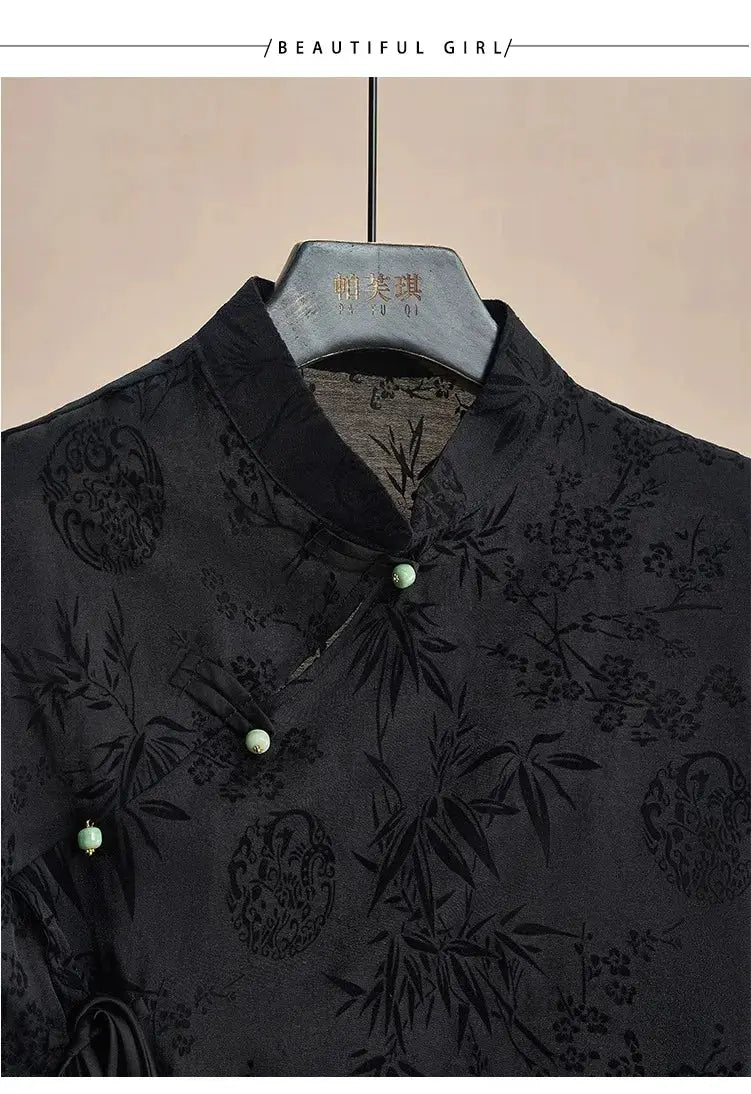 Black jacquard cheongsam-style top with mandarin collar, green frog buttons, and subtle botanical print; short sleeves.