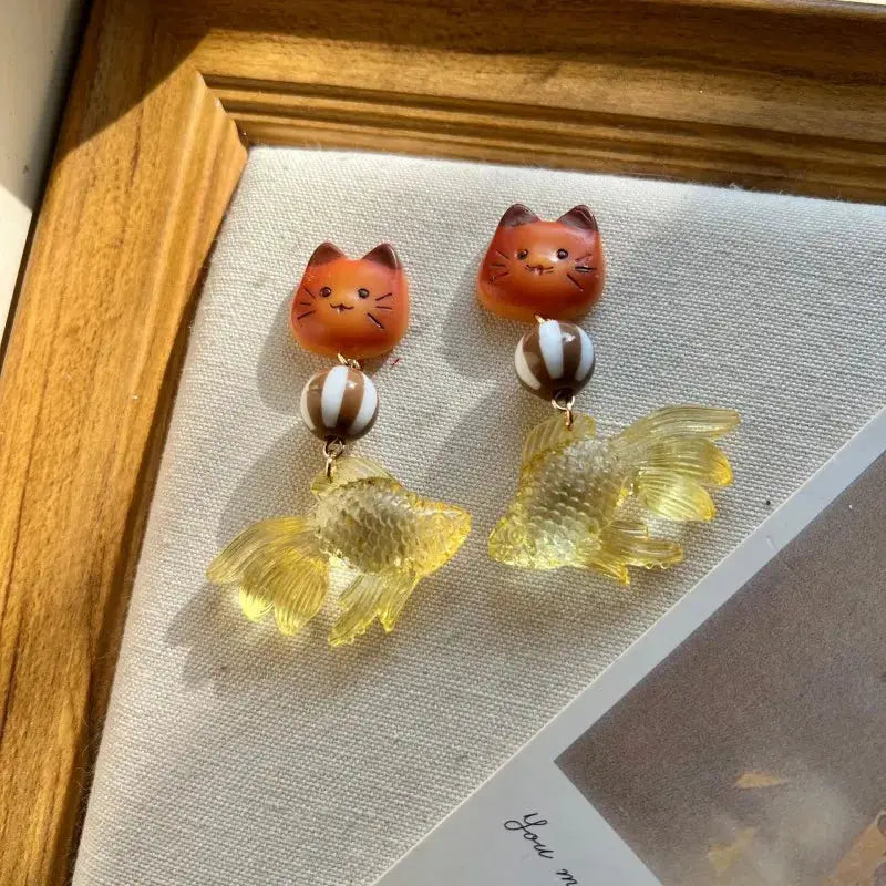 Goldfish drop earrings with yellow translucent fish charms, paired with orange cat-face studs and striped beads