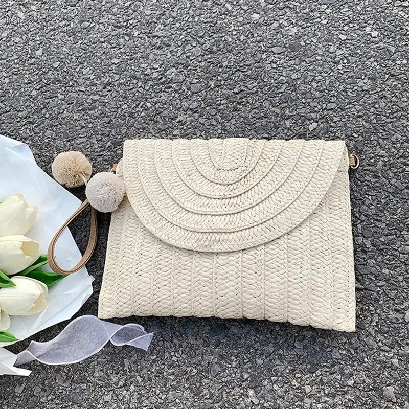 Handmade straw beach crossbody bag with beige woven envelope-style curved flap and pom-pom charm