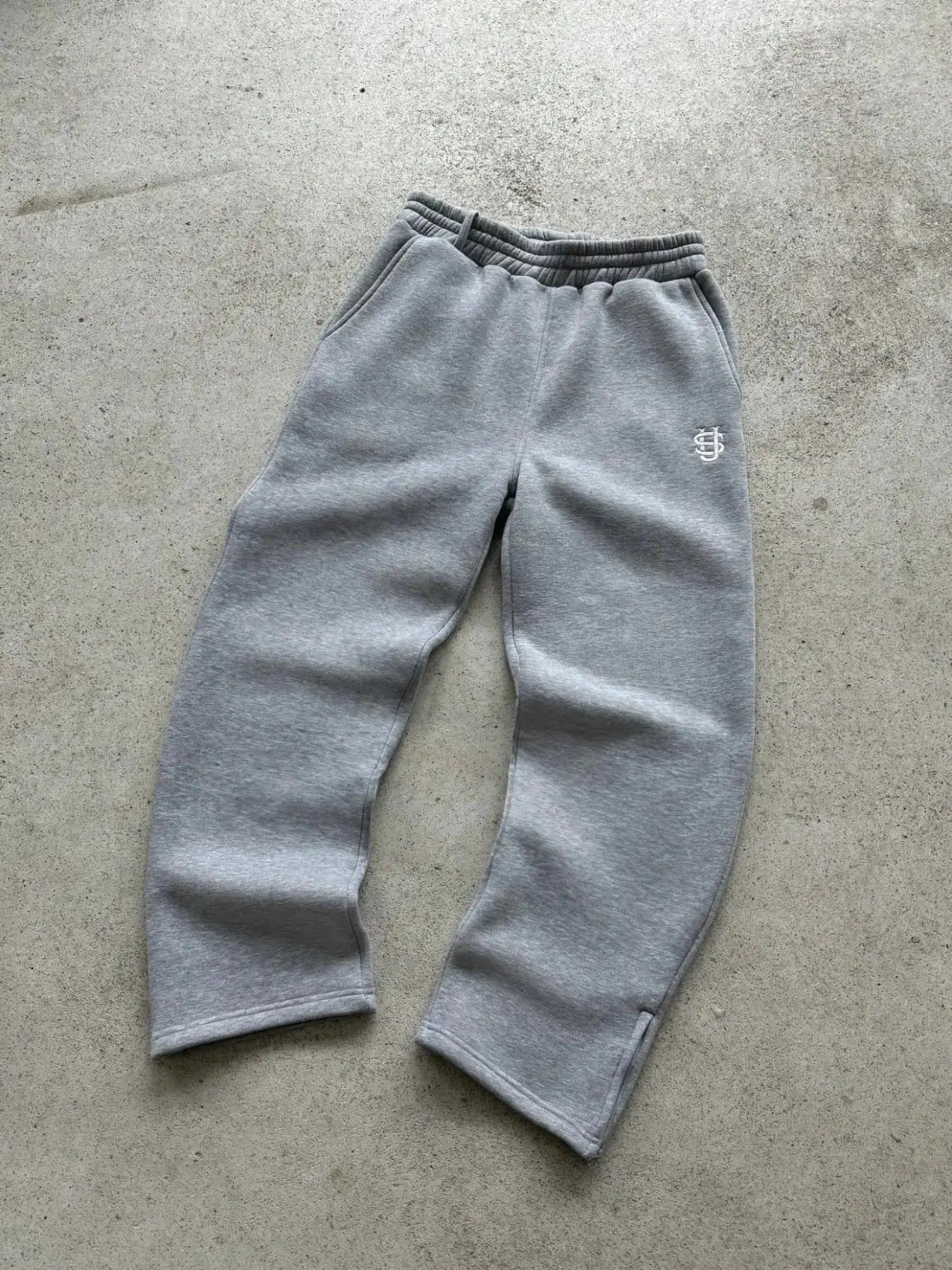 Grey joggers with elastic waistband and side pockets, featuring small white embroidery on the thigh
