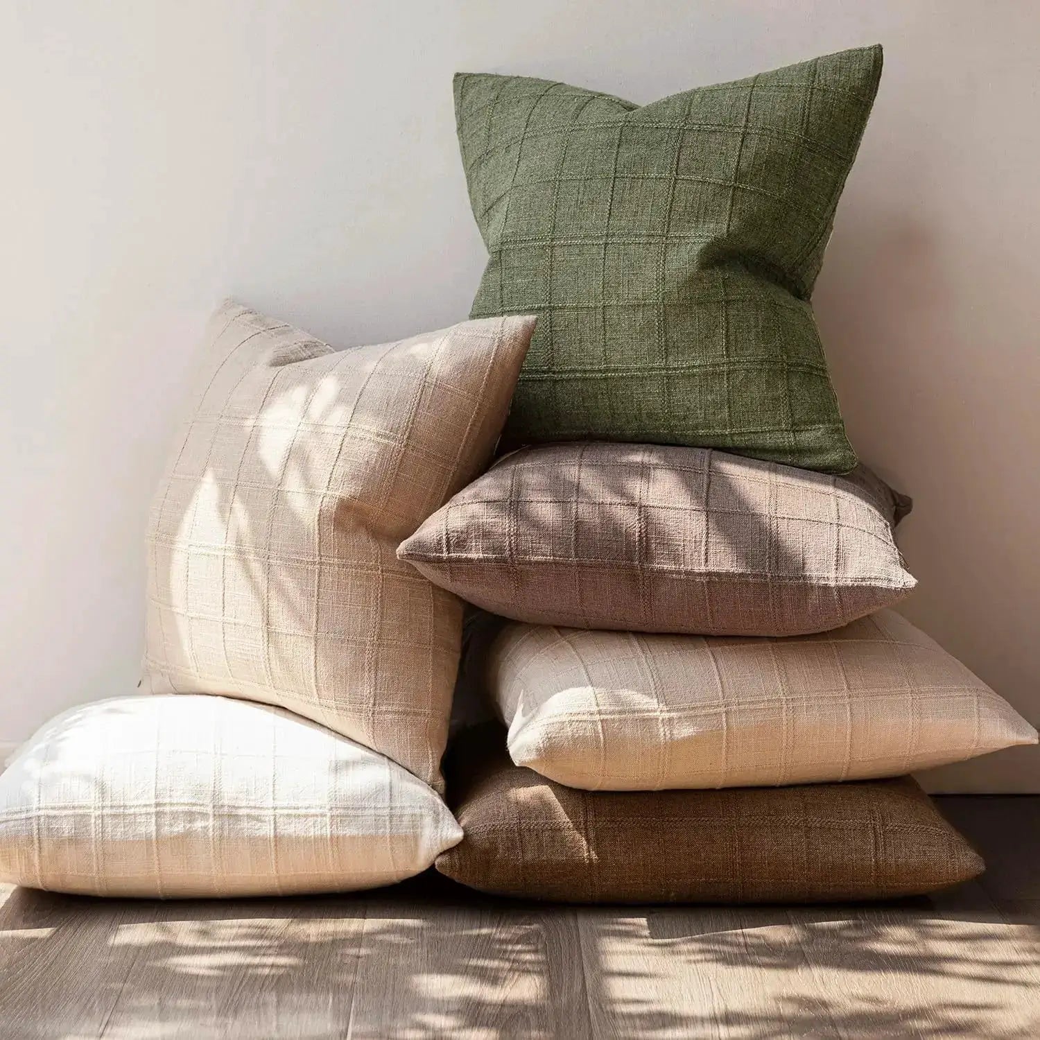 Green square cushion covers set in linen with a grid pattern, stacked on a wooden floor