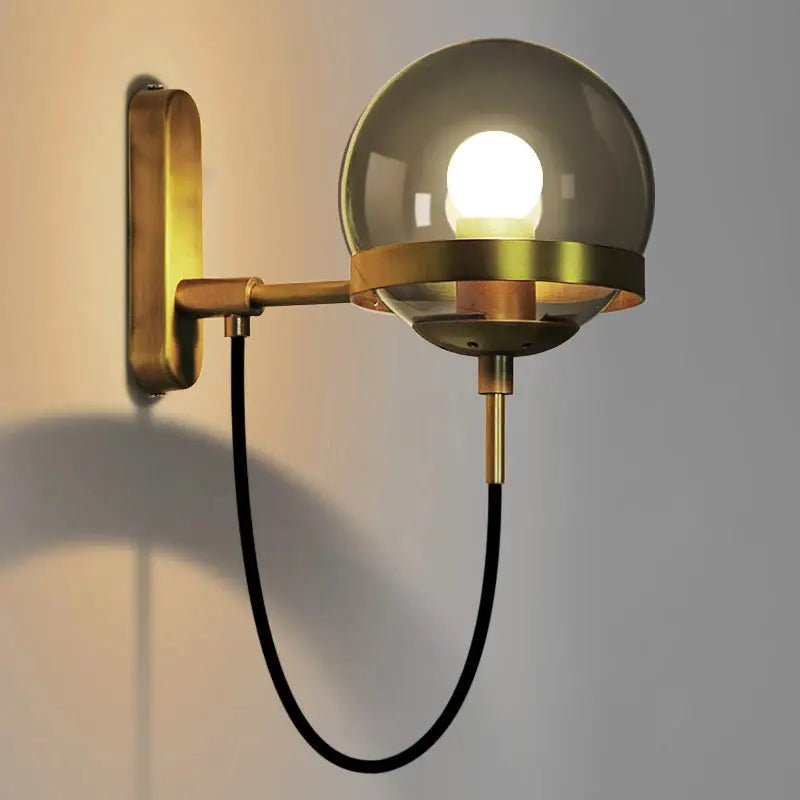 Modern glass ball wall lamp by Simples Market, brass finish with black cord and wall mount.