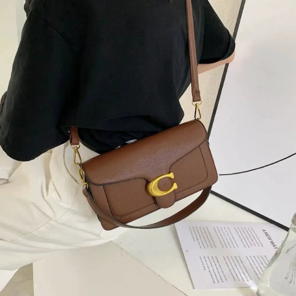 Double-Strap small square crossbody bag by Simples Market, brown leather with gold-tone buckle.