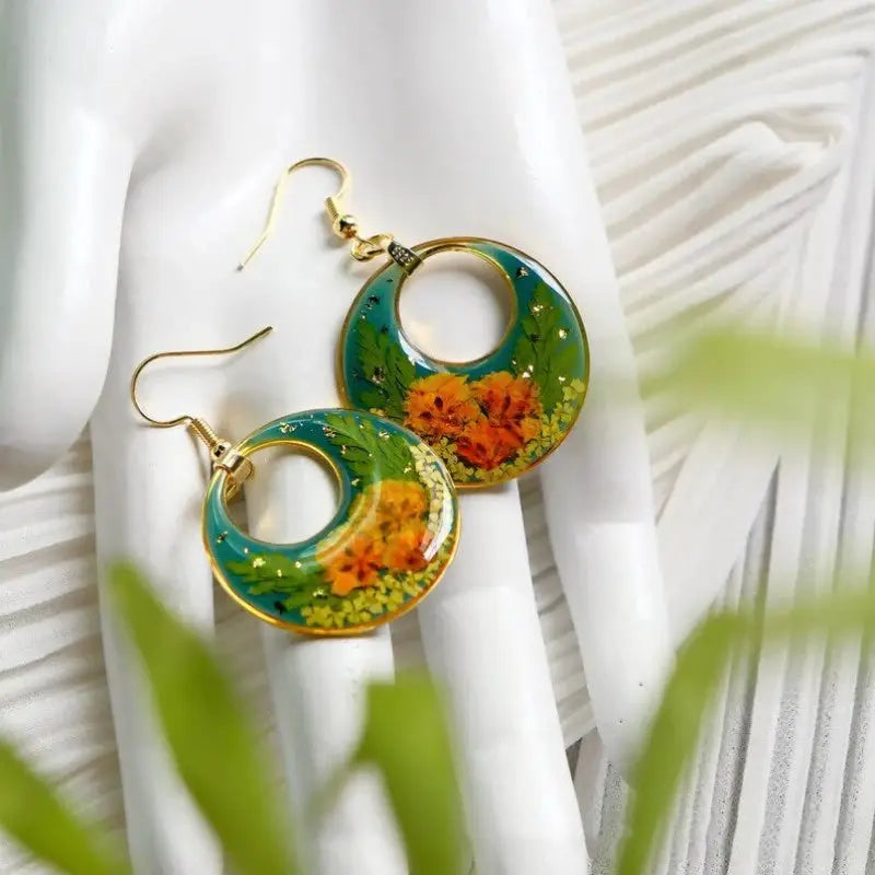 Pressed flower epoxy resin hoop earrings with turquoise background and yellow flowers, gold-tone trim.
