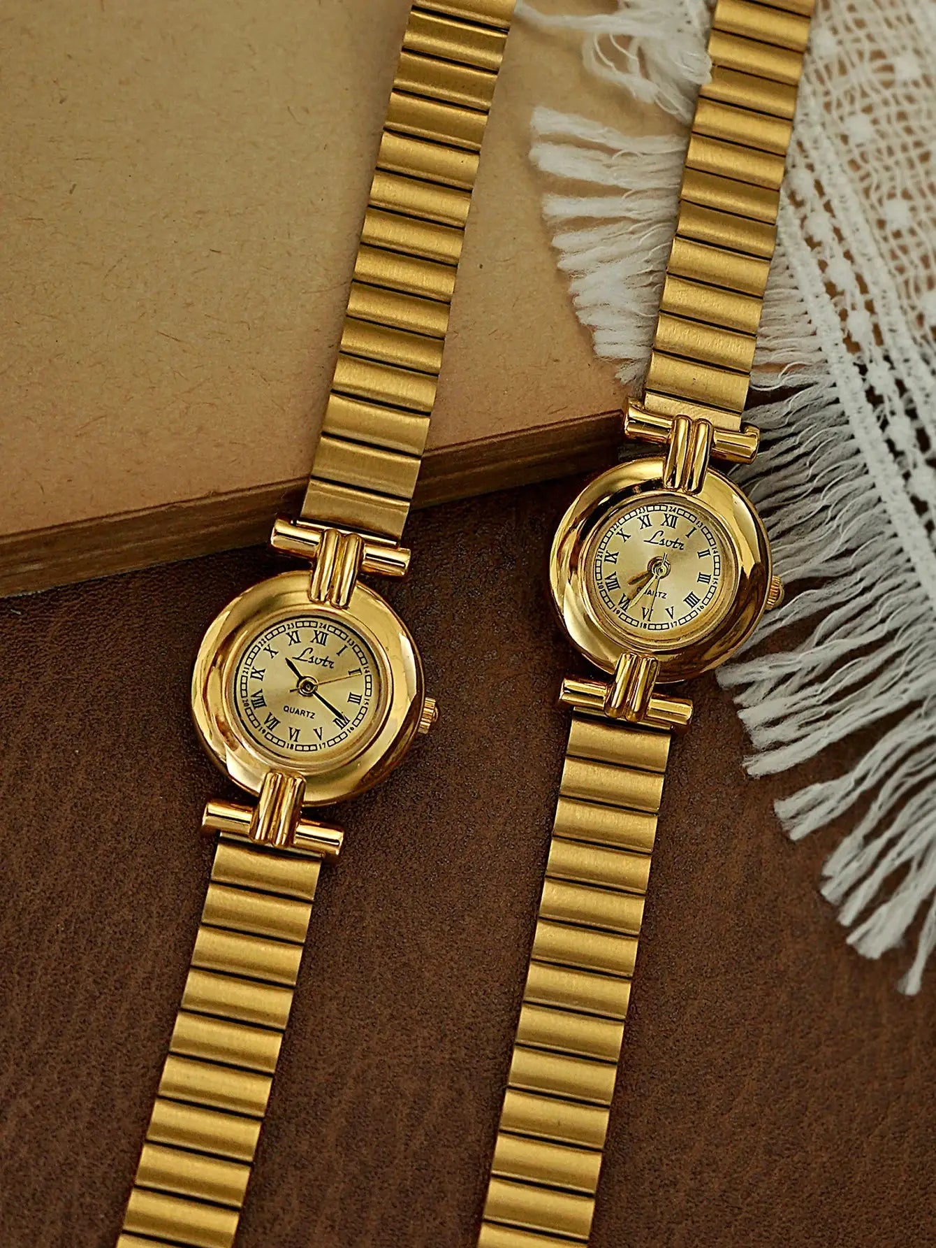 Two gold-tone women's watches with small Roman-numeral dials and metal link bracelets.