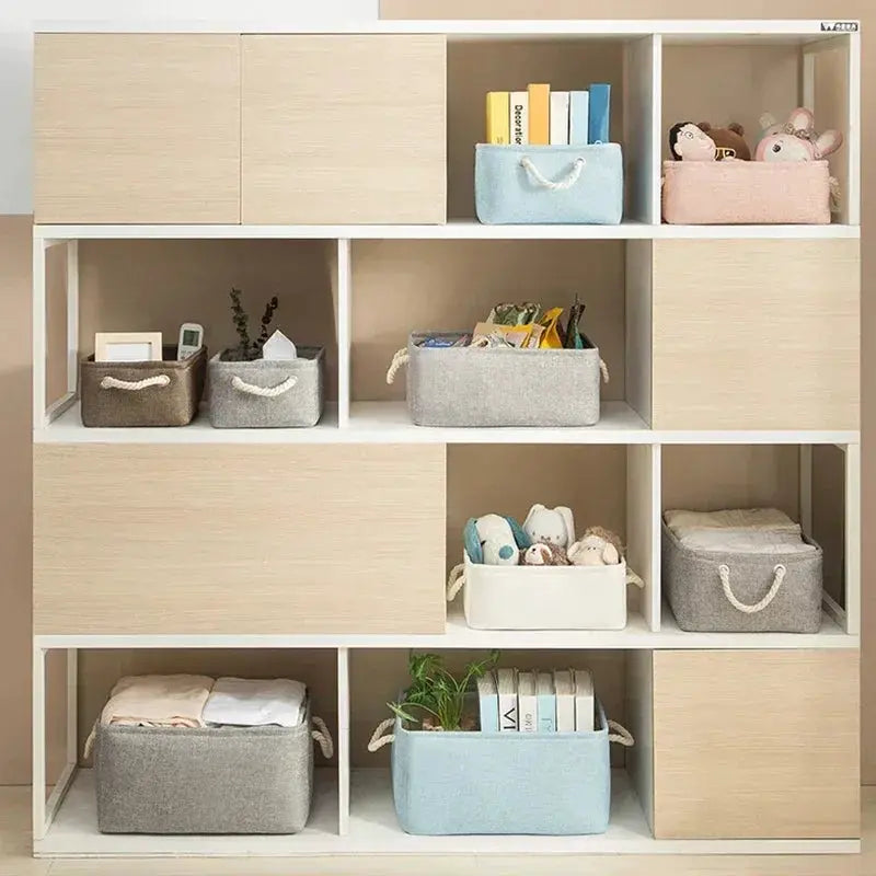 Folding linen fabric storage baskets with rope handles on a white shelving unit.