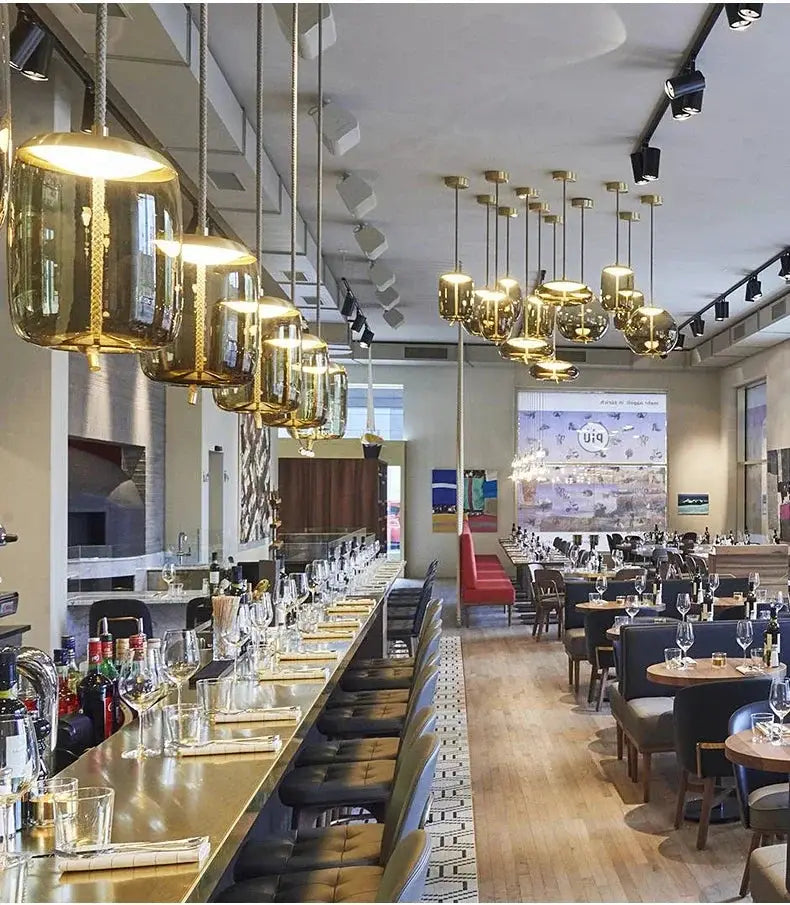 Minimalist pendant lamps over a bar counter in a cafe, hemp-rope suspensions with gold glass shades.
