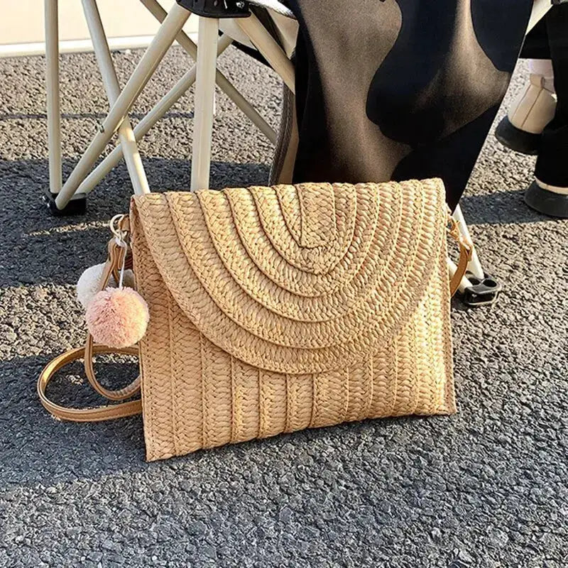 Handmade straw crossbody bag with woven envelope flap, beige color, pink pom-pom charm.