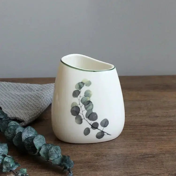 White ceramic bathroom cup with eucalyptus leaf design and green rim.