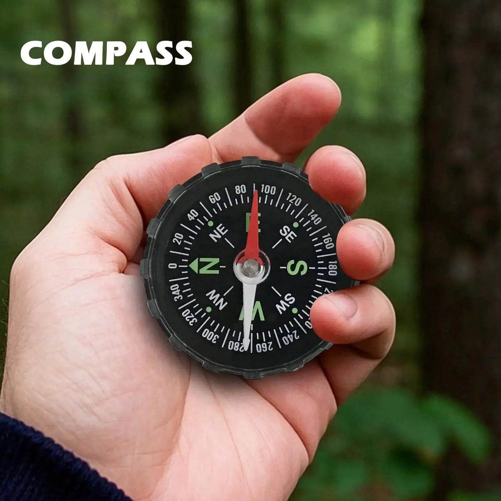 Hiking compass held in hand; black dial with white numerals and red needle outdoors