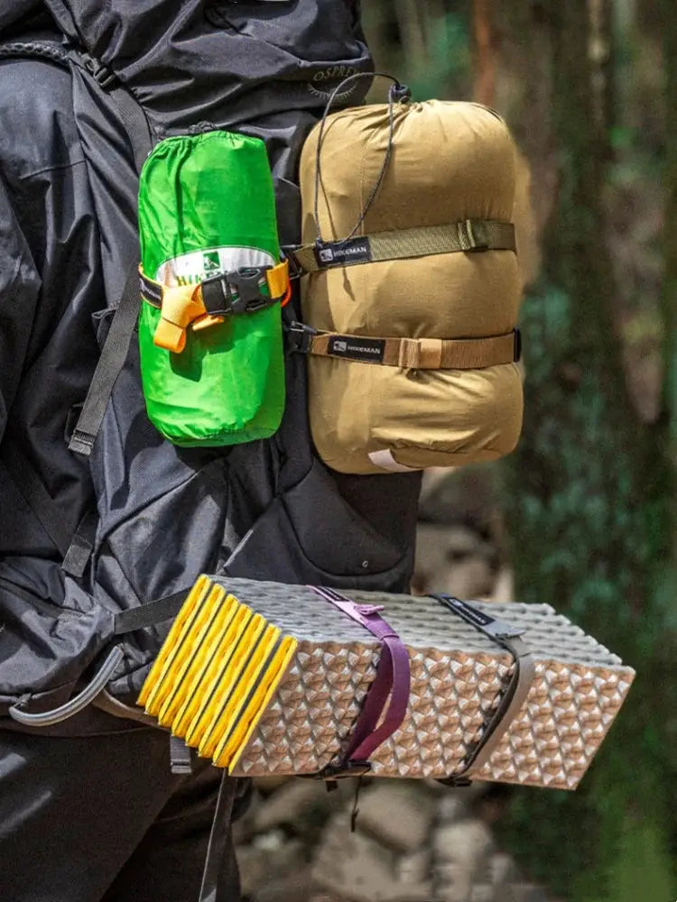 Simples Market tan outdoor packing strap with adjustable plug-in buckle securing camping gear to a backpack