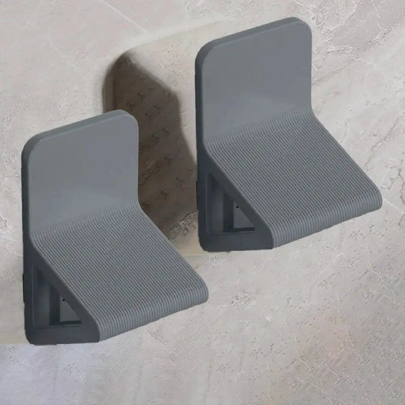 Two wall-mounted gray footstools by Simples Market with ribbed surfaces for foot massage.