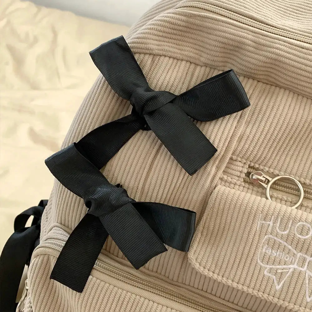 Backpack in beige corduroy with two black grosgrain bows on the straps, college commuting style