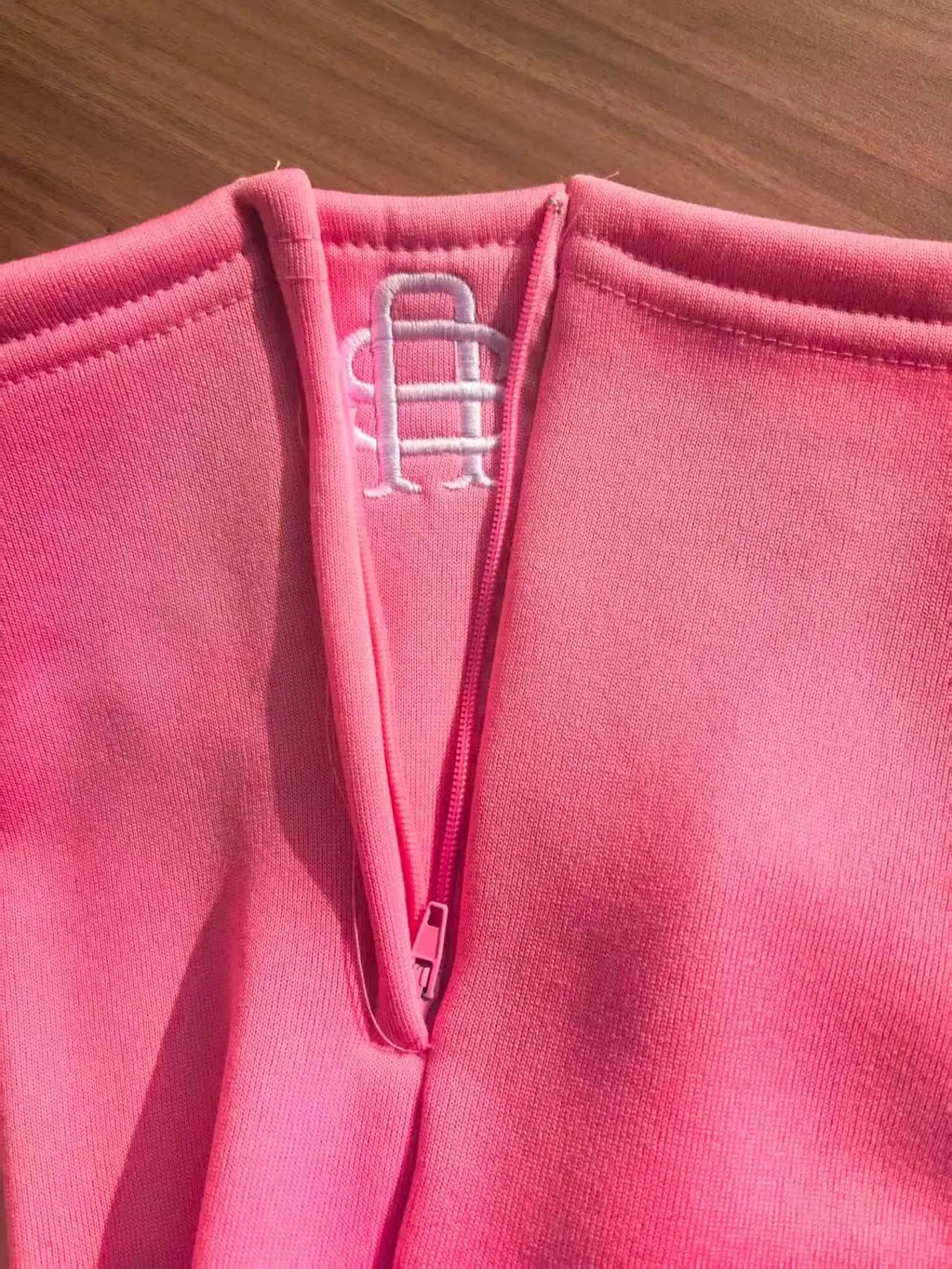 Pink zip-up jacket with a white embroidered logo at the collar, close-up neckline.