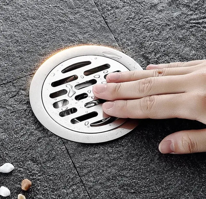 Simples Market stainless steel round floor drain with perforated hair-catching cover on dark bathroom tile