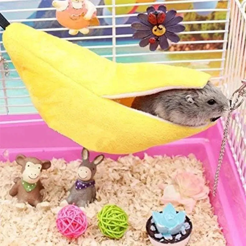 Banana-shaped yellow hamster bed hammock in a cage with bedding and toys.
