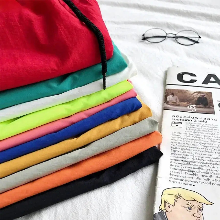 Men's swim trunks stacked in ten assorted colors with a black drawstring beside a newspaper
