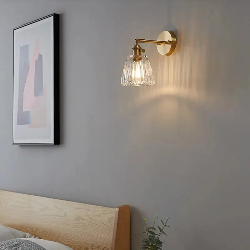 Brass glass wall lamp with ribbed shade, wall-mounted beside a wooden headboard in a Nordic bedroom