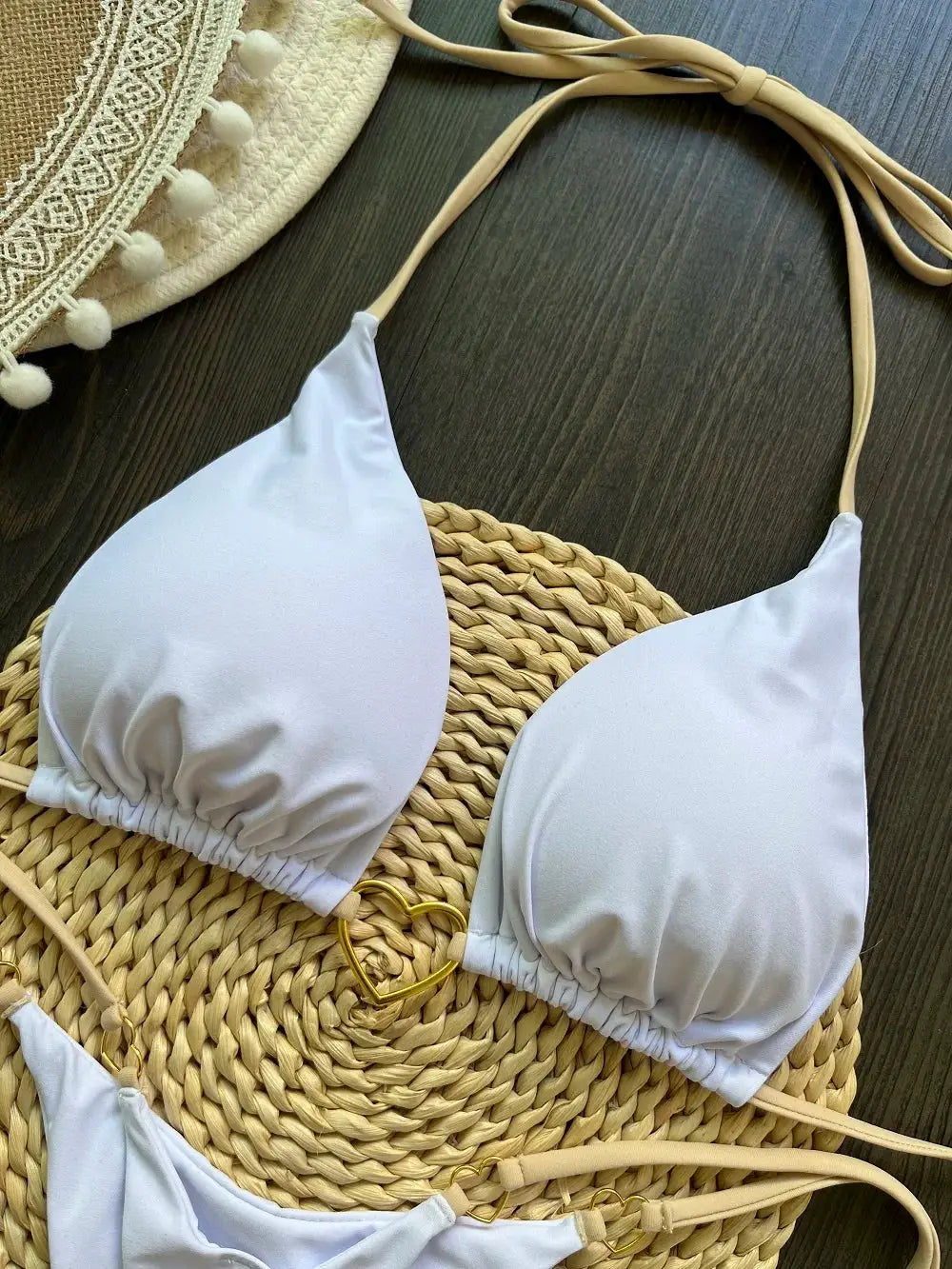 White halter bikini top with beige straps, triangle cups, on a woven straw mat.