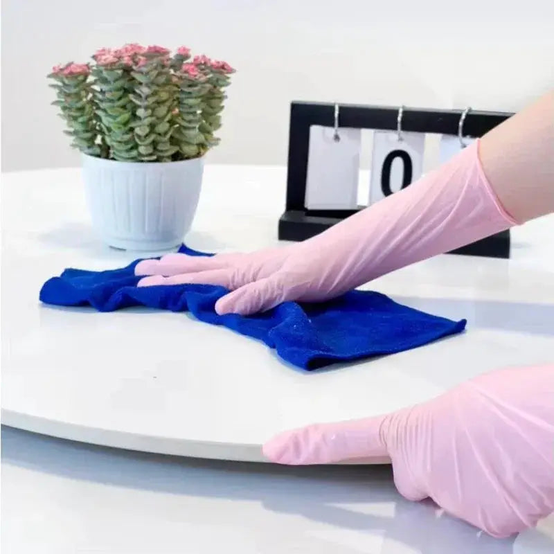 Pink nitrile gloves for household cleaning, shown wiping a blue cloth on a white table