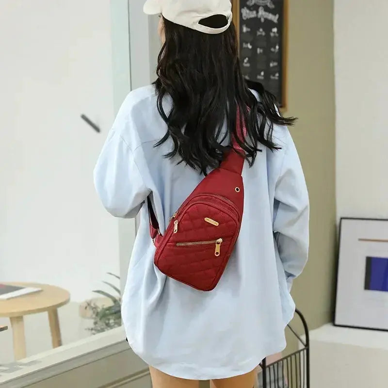 Red quilted crossbody bag with gold zippers worn on the back by a woman in a light-blue shirt