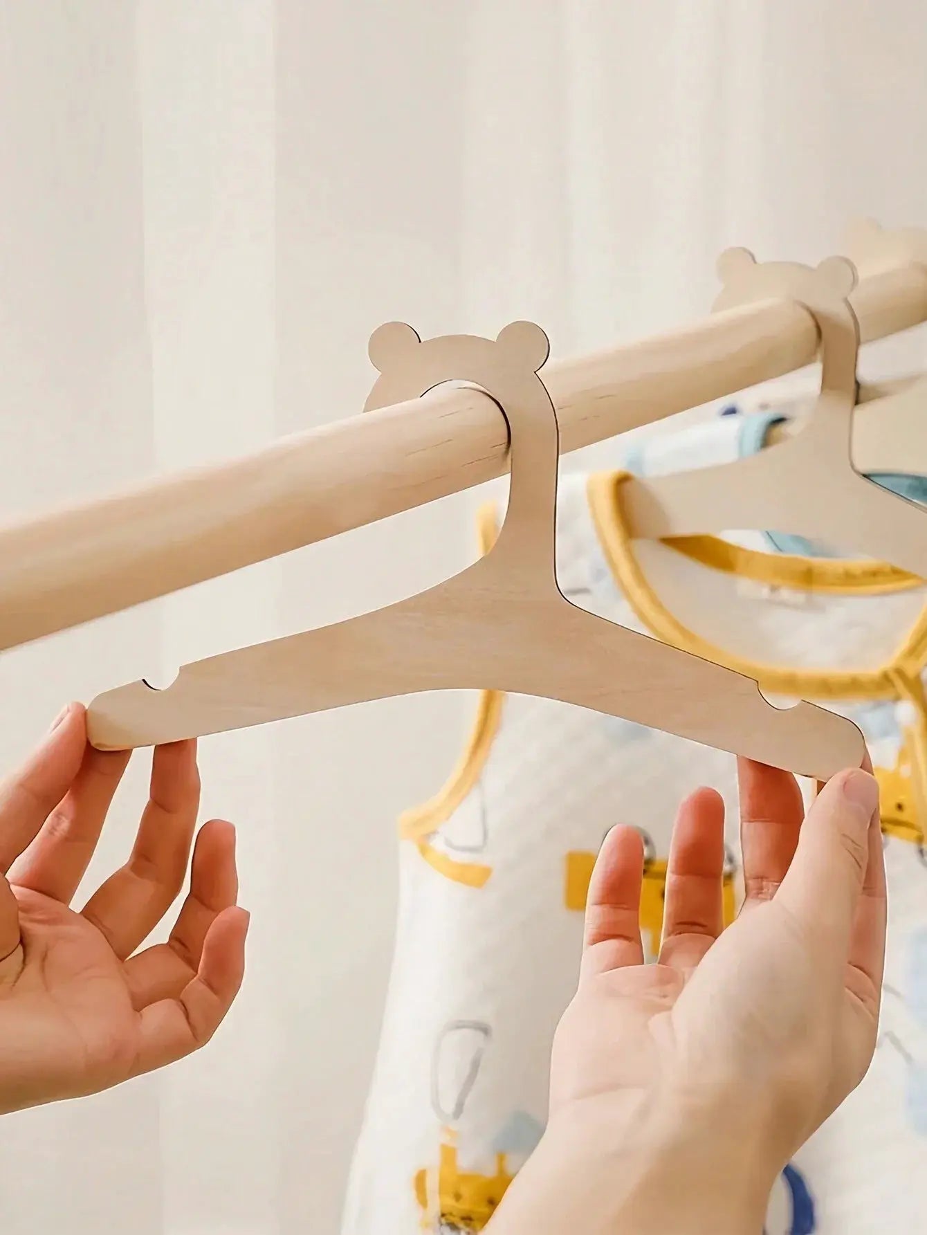 Bear-shaped wooden baby clothes hangers on a natural wood rod; two hangers visible