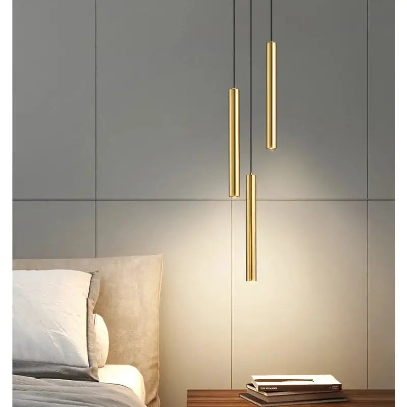 Minimalist bedside pendant lamps, three gold cylindrical LED lights hanging over a gray-paneled bedroom.