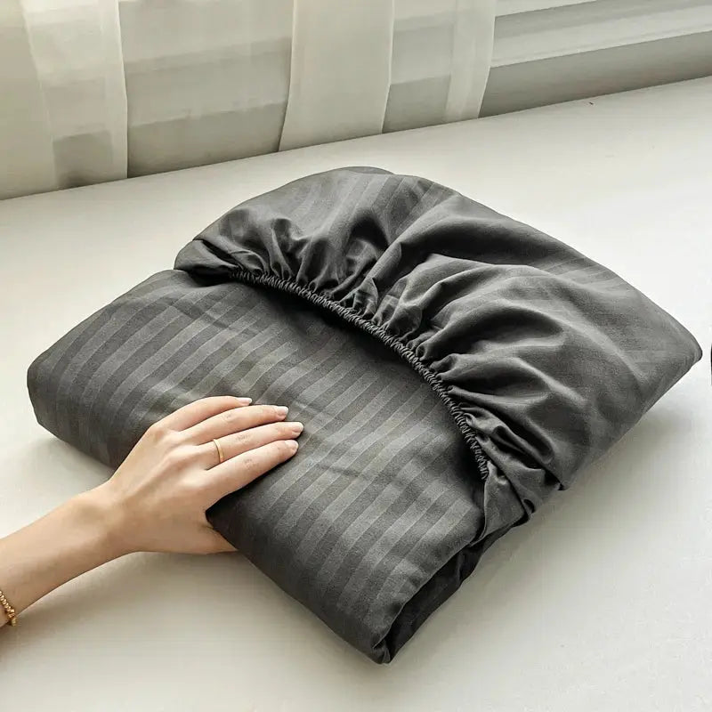 Fitted bed sheet with elastic band in solid dark gray, folded for storage.