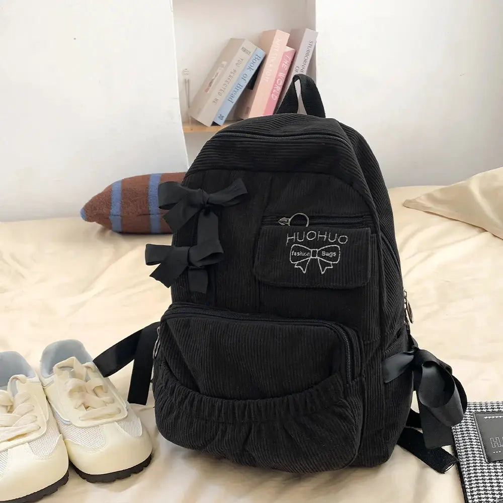 Backpack in black corduroy with bow accents and front pocket for college commuting