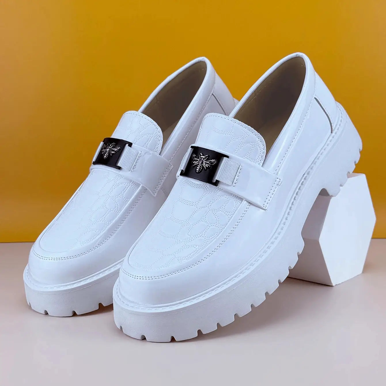 Pair of white leather loafers with chunky sole and bee-emblem buckle, slip-on design