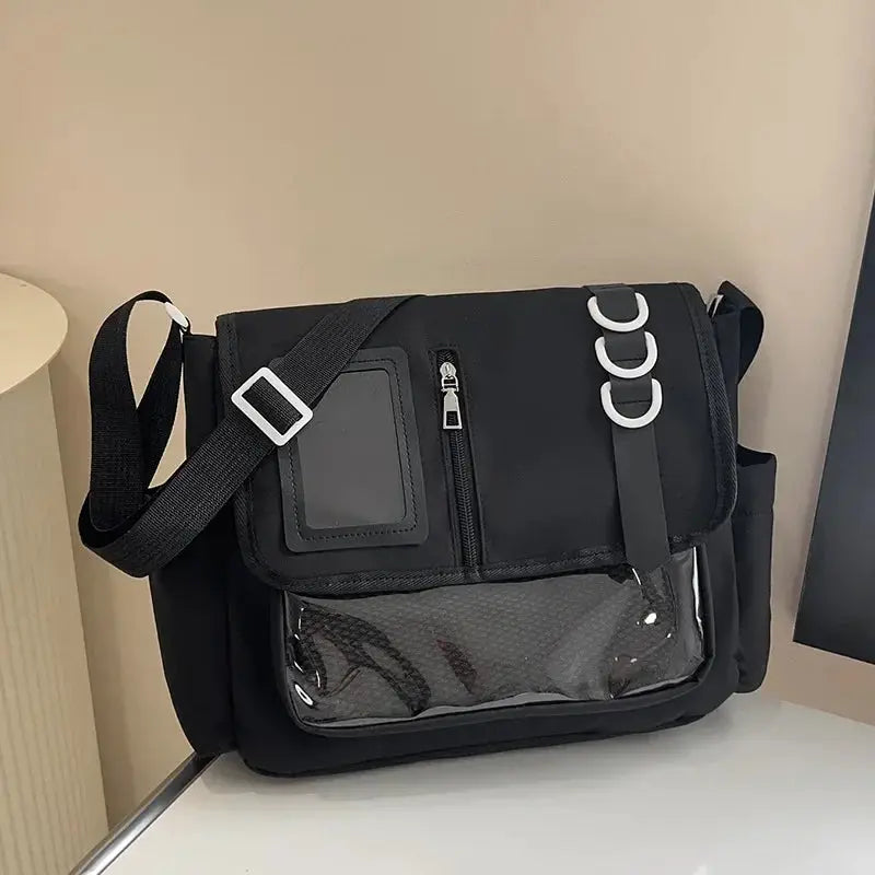 Black ita bag with clear front pocket and zip, adjustable crossbody strap, and white ring accents.