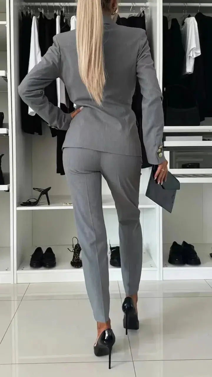 Women's gray office two-piece blazer and trousers suit set, back view with clutch and high heels