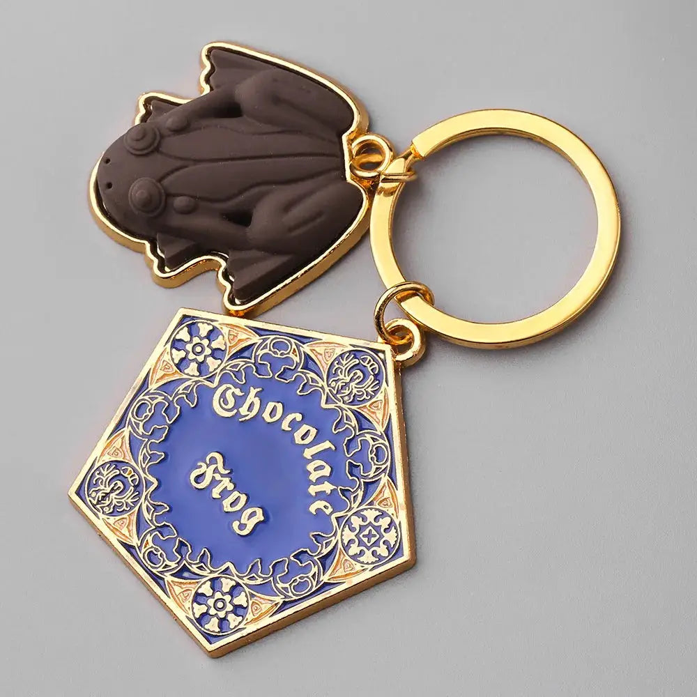 Chocolate Frog keychain by Simples Market; gold-tone metal with brown frog charm and blue ornate panel (two charms)