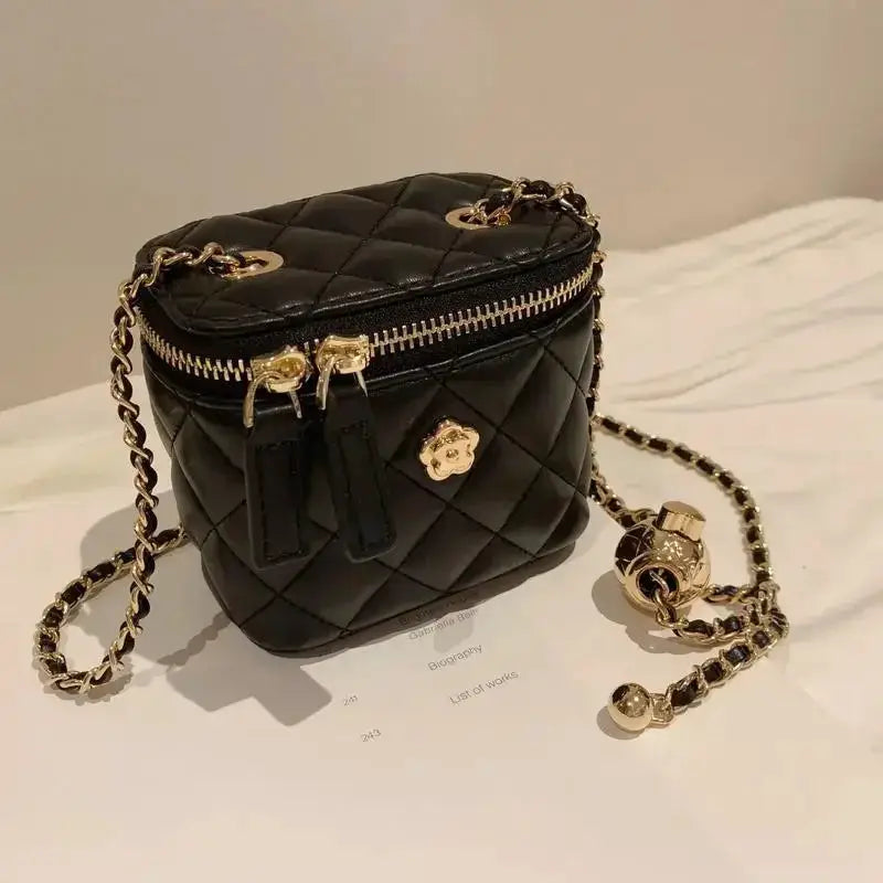 Simples Market mini black quilted shoulder bag with gold chain strap, top zipper, and floral charm.