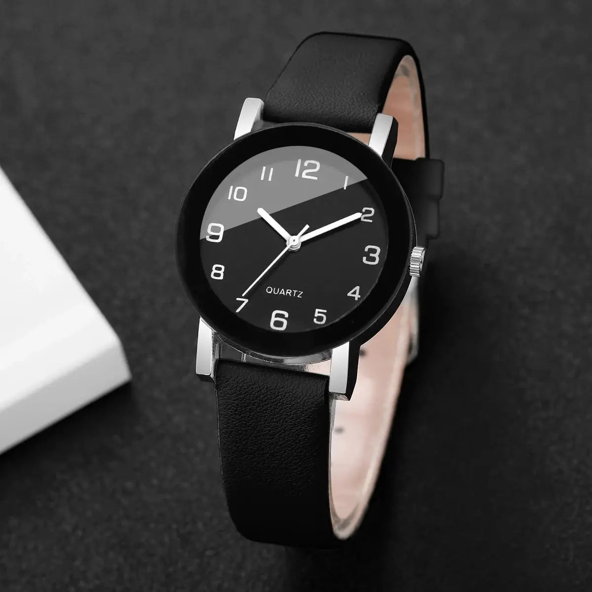 Wristwatch with black leather strap and round black dial featuring white Arabic numerals and silver case.