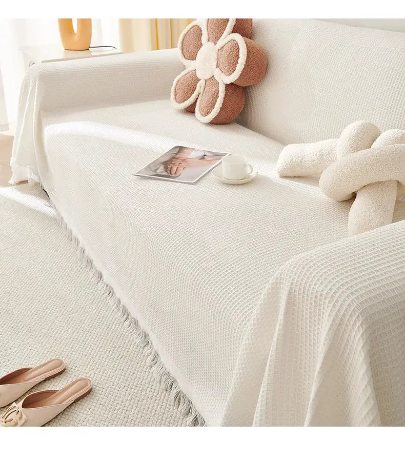 Cream sofa throw blanket in wind cotton yarn with fringe edge on a white sofa.