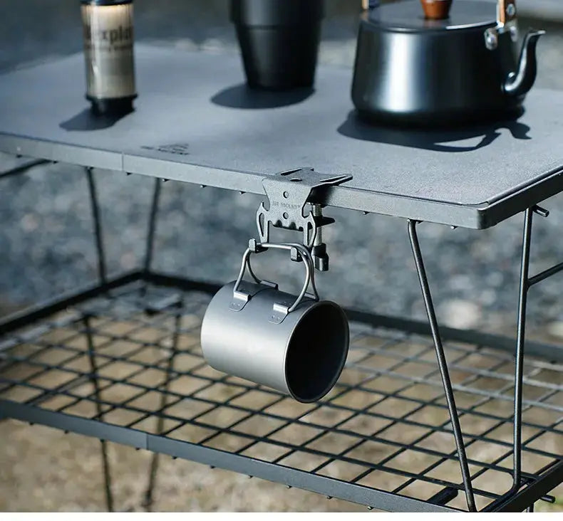 Gas canister hook for camping; gray metal hanging hook with hanging plate and built-in bottle opener under a camping table.