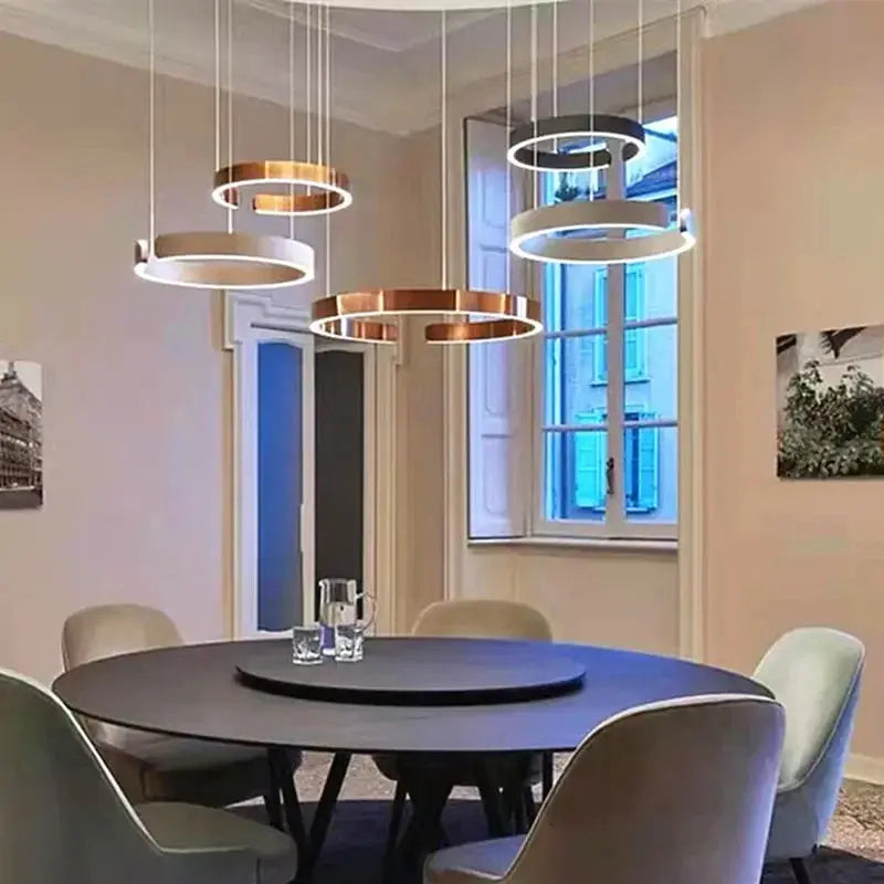 Five Nordic ring LED pendant lamps in black, white, and gold finishes hanging over a round dining table