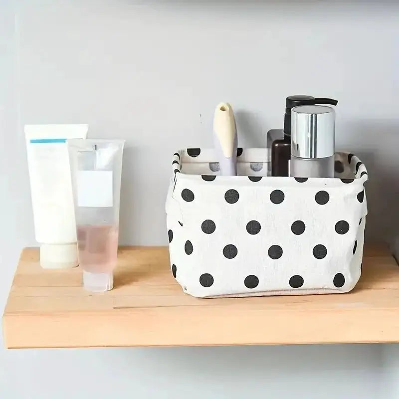 Foldable canvas storage basket with handle; white fabric with black polka dots on a wooden shelf