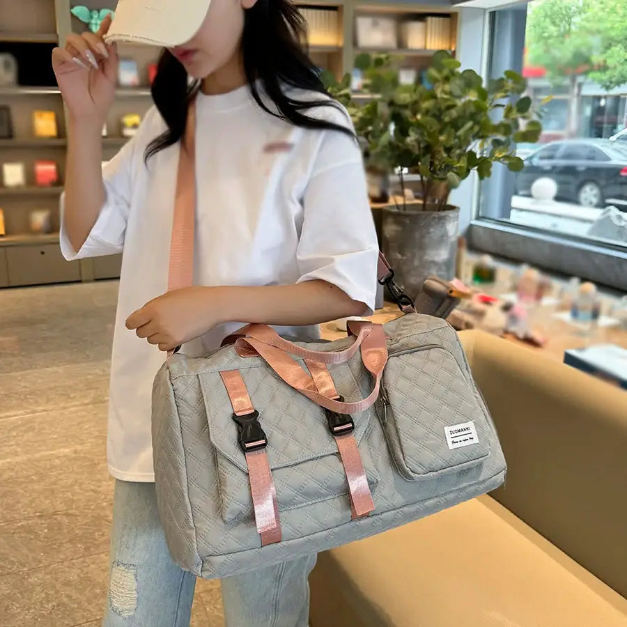 Durable nylon travel duffle bag in gray quilted fabric with pink straps and front pocket, carried by a woman.