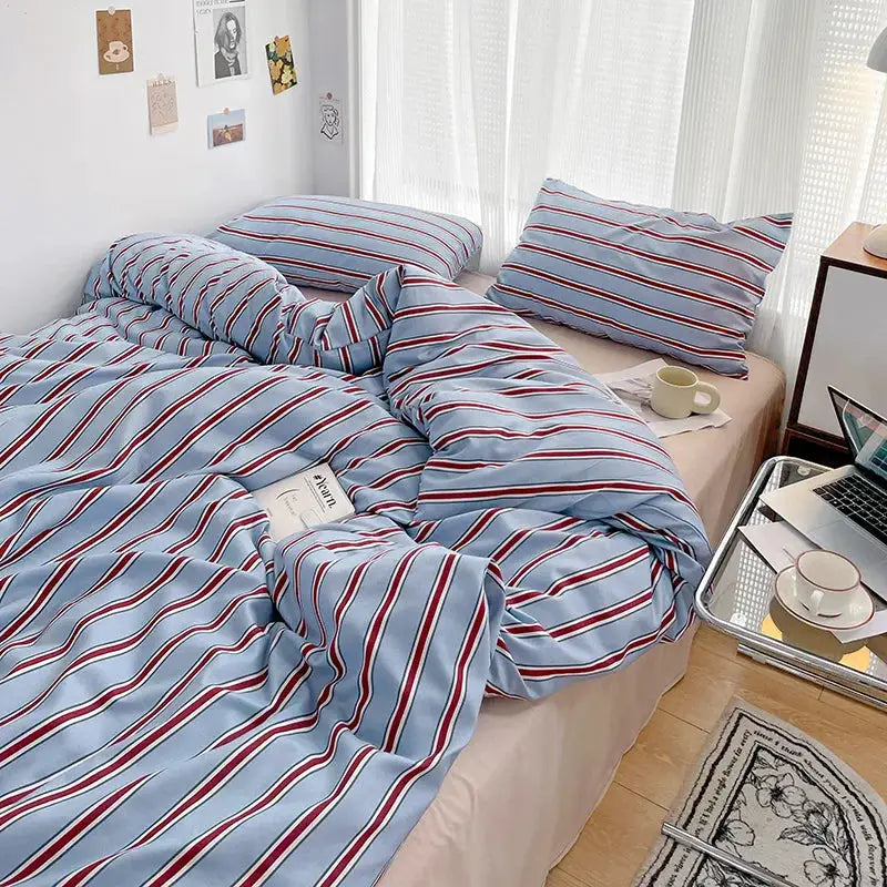 Duvet cover and four-piece sheet set by Simples Market in blue and red striped washed cotton on bed
