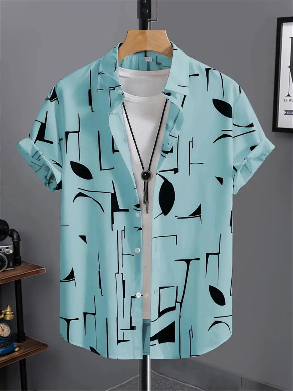 Men's turquoise short-sleeve shirt with black abstract geometric print on display.